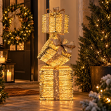 Tre pacchi regalo luminosi dorati con micro LED a luce calda ambientati all'esterno per Natale