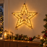 Stella luminosa Garden Team da 58 cm con micro LED bianco caldo, appesa alla parete sopra una composizione natalizia.