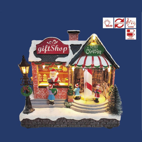 Negozio natalizio in miniatura con insegna gift shop, vetrina illuminata con Babbo Natale e bambini che osservano decorazioni sotto la neve su sfondo blu.