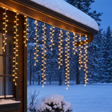 Tenda luminosa Ice Light con mini LED bianco caldo appesa alla grondaia di una casa in legno durante una serata invernale.