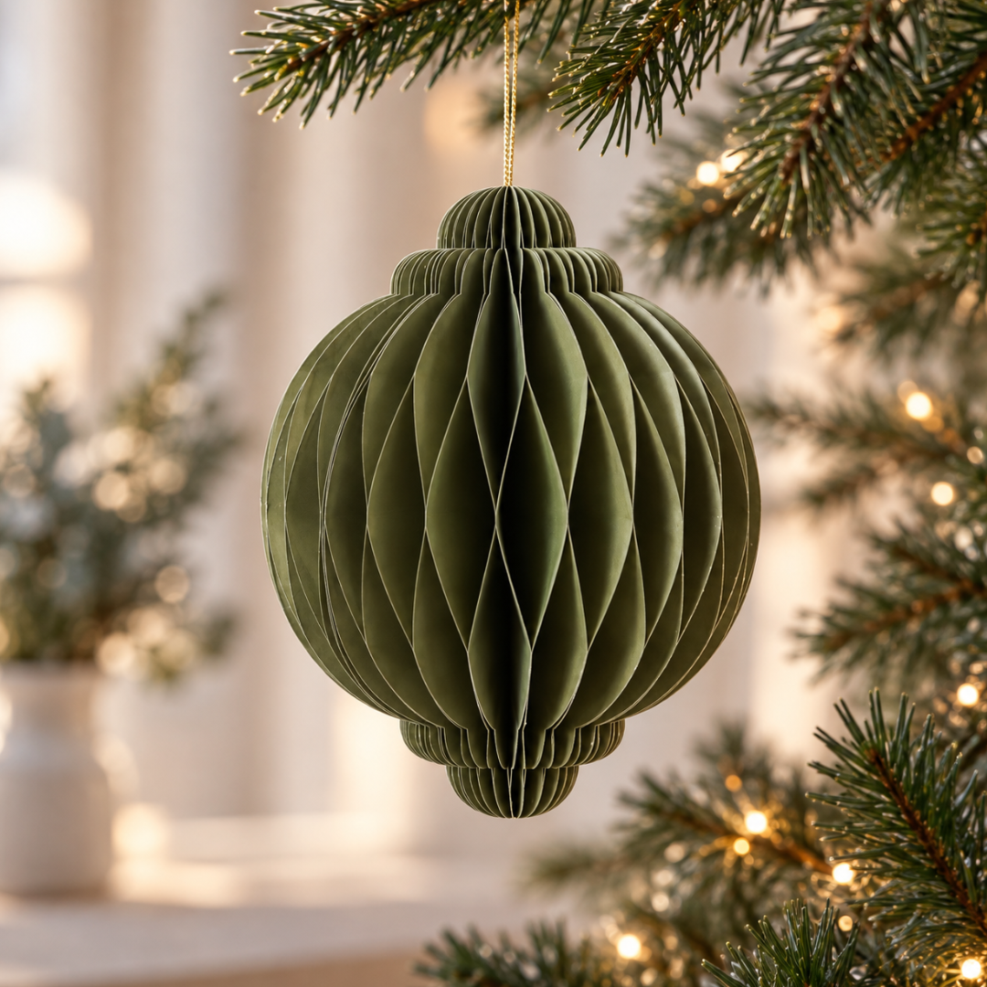 Pallina di Natale verde oliva in carta pieghettata appesa all’albero tra luci natalizie calde