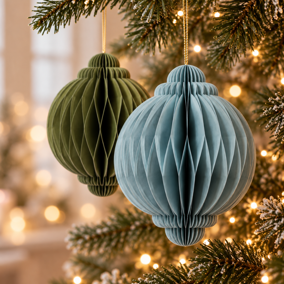 Palline di Natale in carta pieghettata azzurra e verde oliva appese ai rami dell’albero illuminato