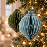 Palline di Natale in carta pieghettata azzurra e verde oliva appese ai rami dell’albero illuminato