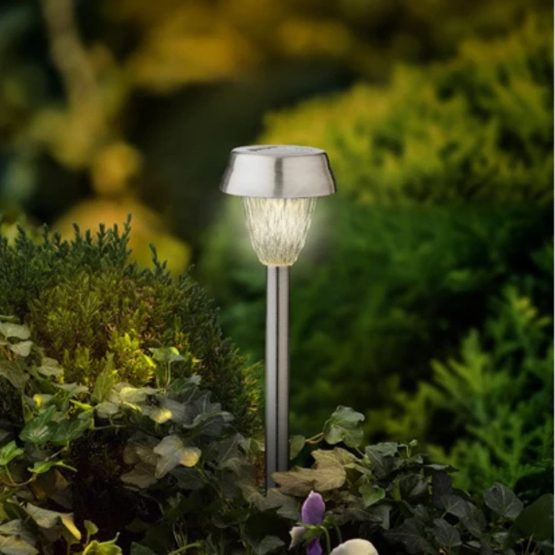 Lampada solare a paletto accesa in un’aiuola tra piante e cespugli di un giardino