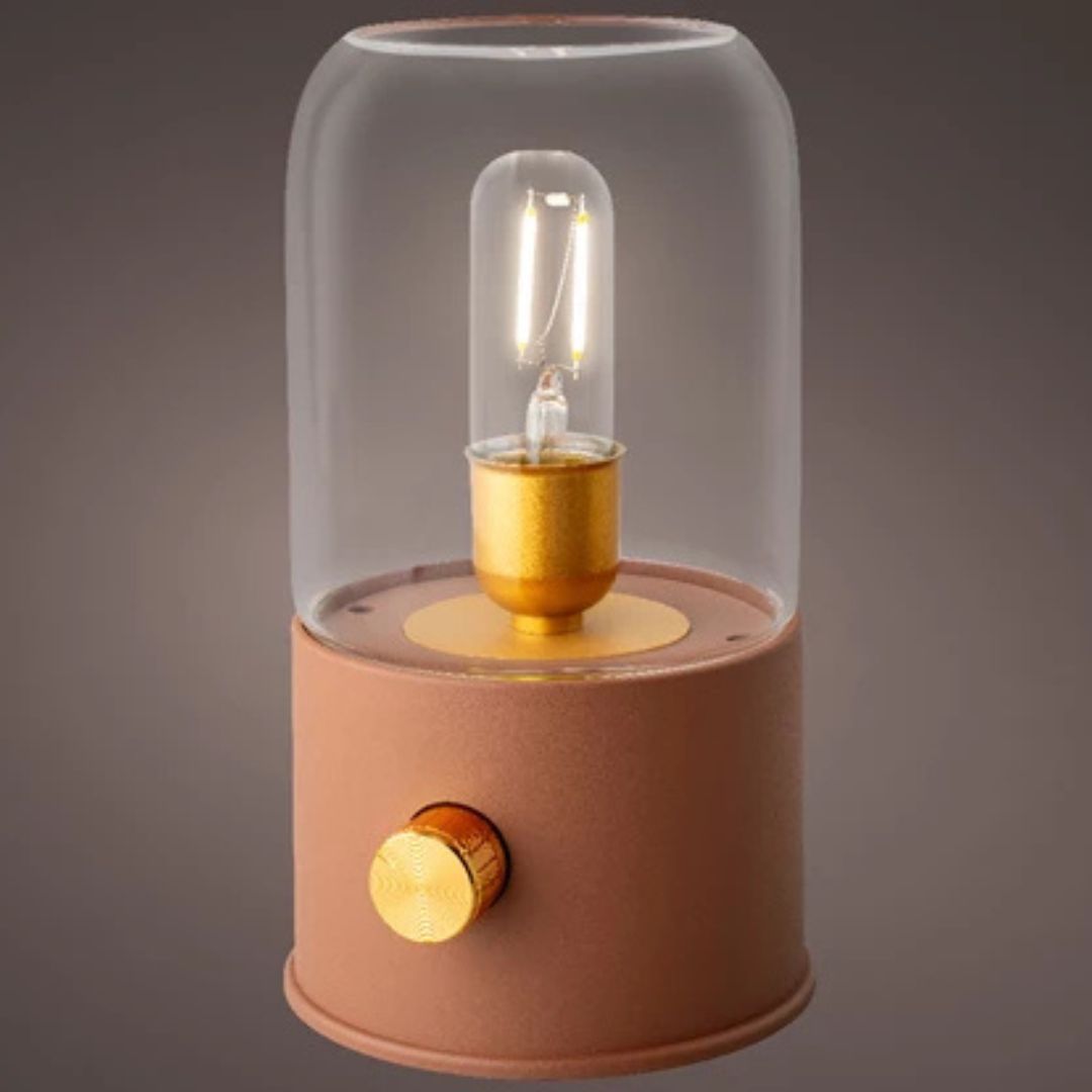 Lampada da tavolo stile vintage con base color terracotta, vetro trasparente e manopola dorata, ambientata