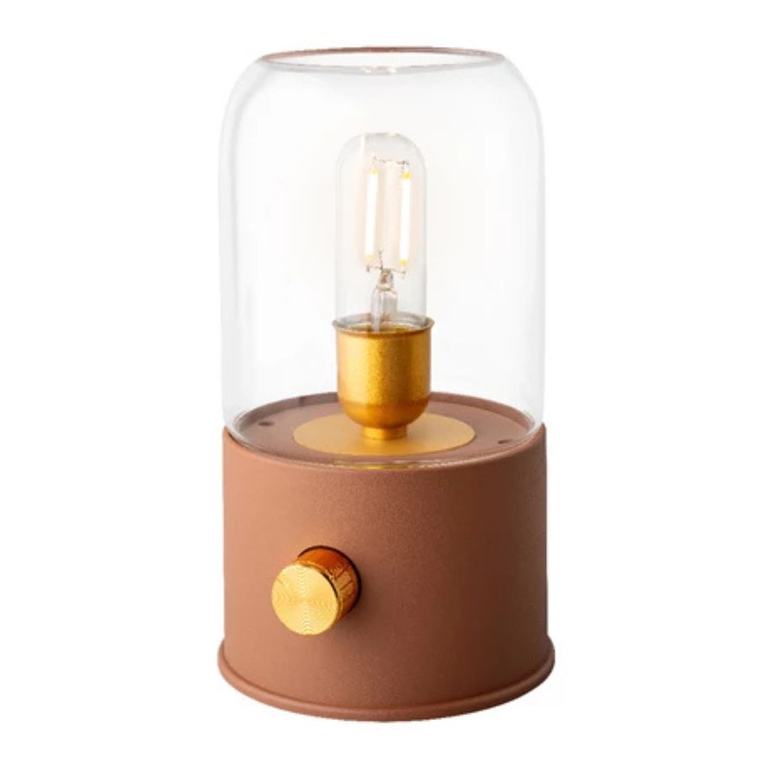 Lampada da tavolo con vetro trasparente e base color terracotta, luce accesa, fondo bianco