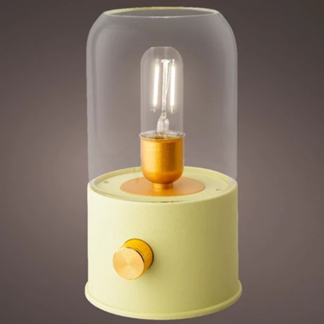 Lampada da tavolo con vetro trasparente e base lime, luce calda accesa, sfondo grigio