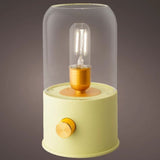 Lampada da tavolo con vetro trasparente e base lime, luce calda accesa, sfondo grigio