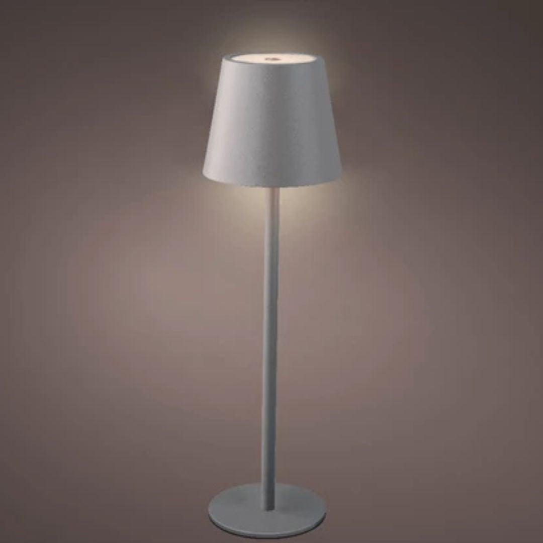 Lampada da tavolo da interni in metallo grigio con luce accesa, fondo scuro.