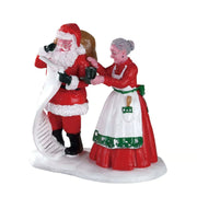 Personaggi Lemax con Babbo Natale che consulta la lista mentre Mrs. Claus gli porge una tazza di cioccolata calda.