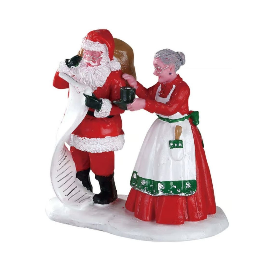 Personaggi Lemax con Babbo Natale che consulta la lista mentre Mrs. Claus gli porge una tazza di cioccolata calda.