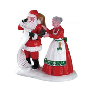 Personaggi Lemax con Babbo Natale che consulta la lista mentre Mrs. Claus gli porge una tazza di cioccolata calda.