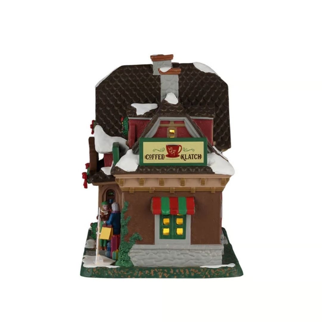 Coffee Klatch Lemax visto di lato, con tetto innevato, insegna della caffetteria, finestra illuminata e tenda a righe rosse e verdi.