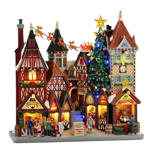 Grande scena natalizia Lemax con edifici in stile tradizionale, bancarelle illuminate, albero di Natale decorato, torre con orologio e slitta di Babbo Natale con renne sullo sfondo.