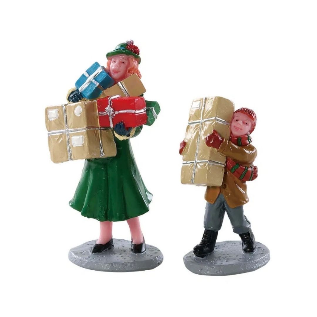 Coppia di personaggi Lemax con numerosi pacchi regalo tra le braccia, vestiti con abiti invernali nei toni del verde, marrone e rosso.