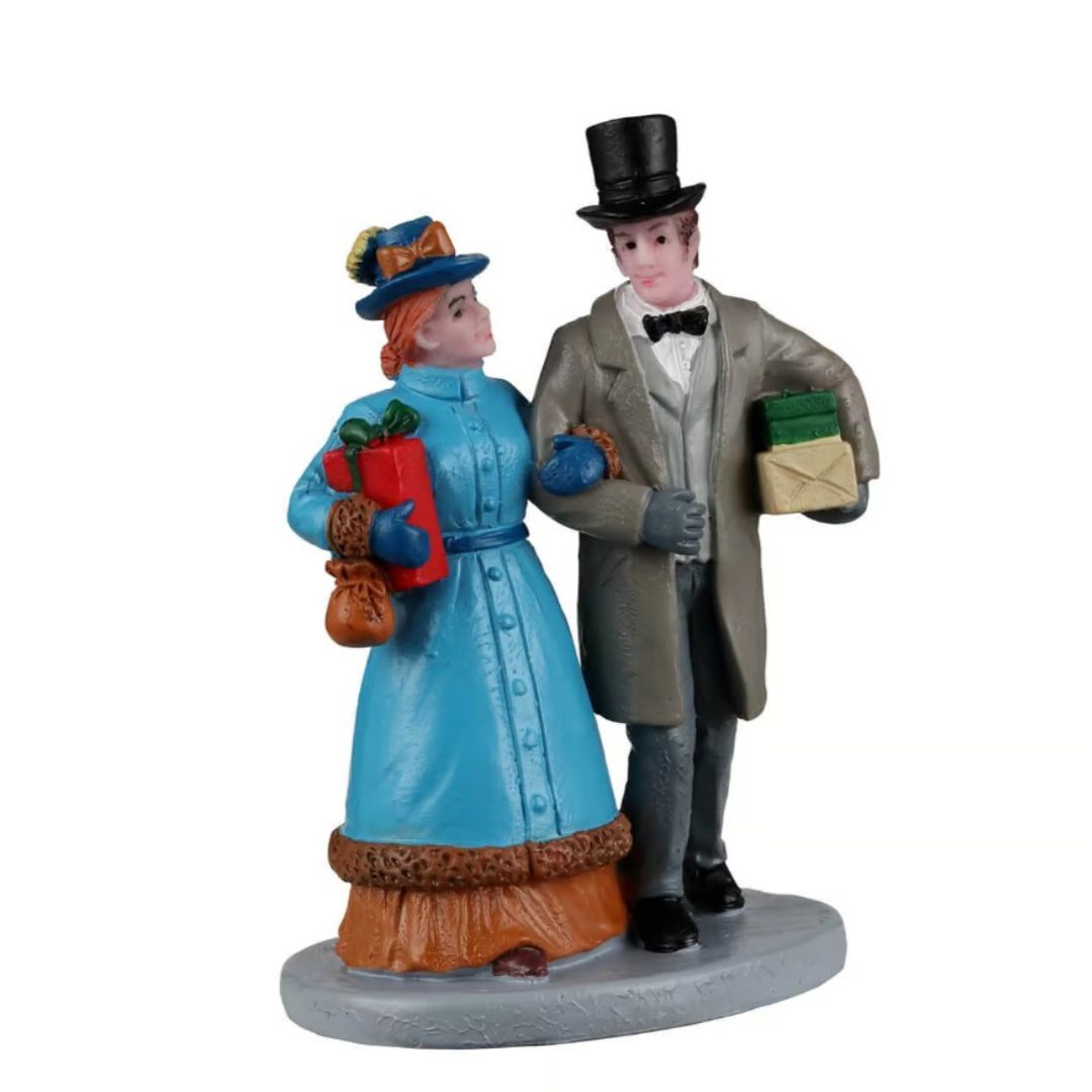 Personaggi Lemax con coppia in abiti eleganti invernali, entrambi con pacchetti regalo tra le braccia.