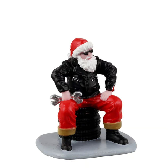 Babbo Natale in giacca nera, occhiali da sole e pantaloni rossi, seduto su una pila di pneumatici con una chiave inglese.