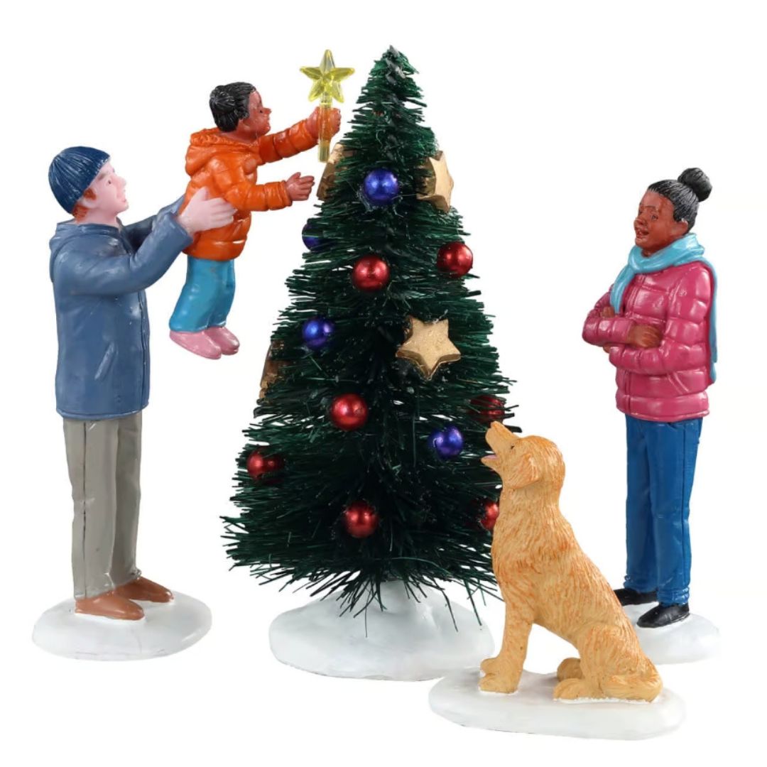 Final Touch Lemax con famiglia che decora l’albero di Natale: adulto solleva un bambino per posizionare la stella in cima, mentre una donna e un cane osservano la scena.