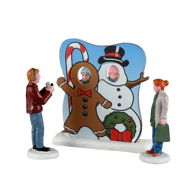Scena Lemax con due bambini che posano con il volto nelle sagome di un omino di pan di zenzero e di un pupazzo di neve, mentre due adulti li fotografano.