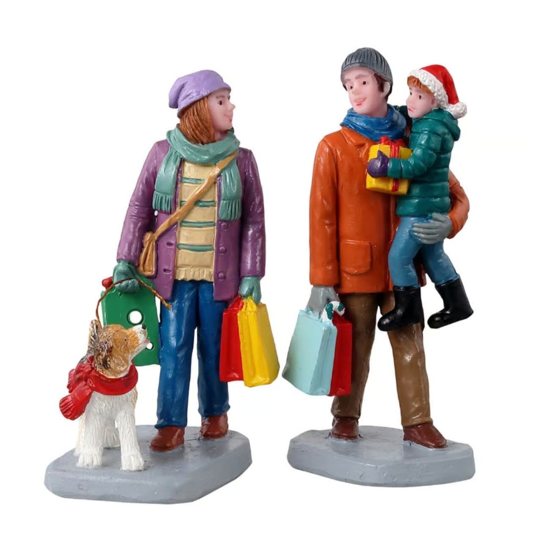 Holiday Shoppers con famiglia durante lo shopping natalizio: donna con borse e cane al guinzaglio, uomo con sacchetti e bambino in braccio con regalo.