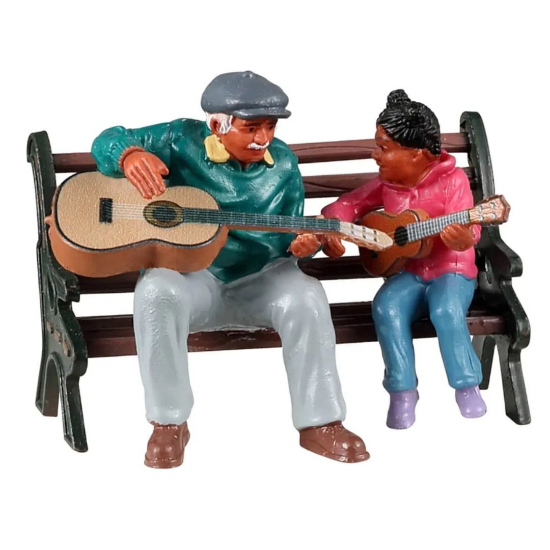 Statuetta con un uomo e bambina seduti su una panchina mentre suonano insieme la chitarra.