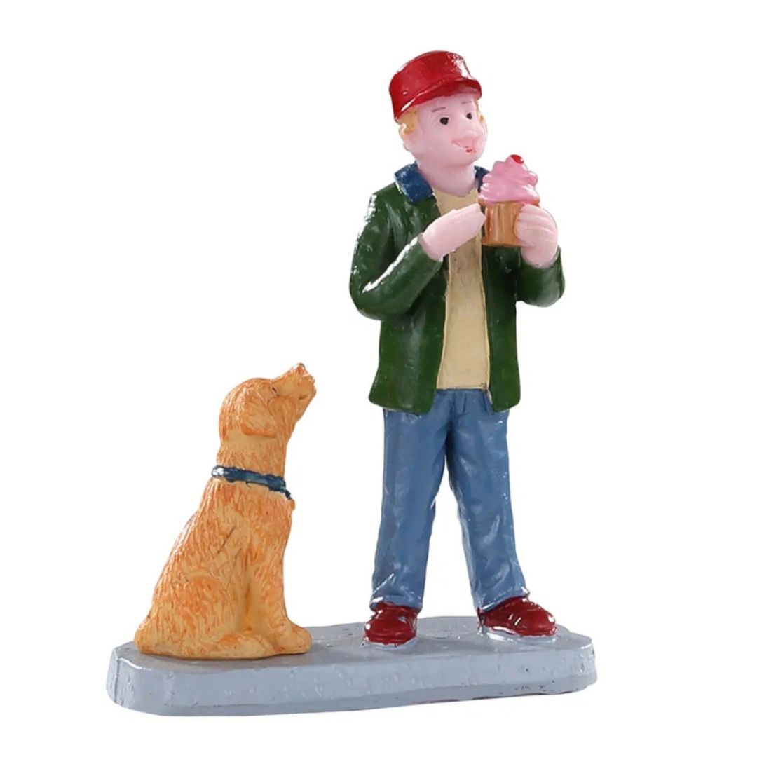 Personaggi Lemax con ragazzo che tiene un cupcake rosa mentre un cane seduto accanto a lui lo osserva con attenzione.