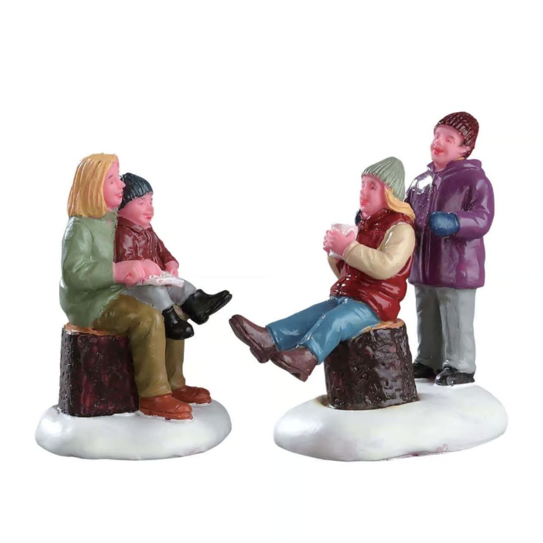 Due madri con le loro figlie in abiti invernali riunite sulla neve, due sedute su tronchi e due in piedi mentre conversano.