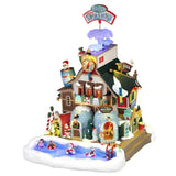 Edificio natalizio Lemax illuminato con centro termale di Babbo Natale, piscina esterna tra la neve, sauna, torre con termometro e dettagli colorati a tema Polo Nord.