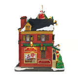 Tidings and Joy Toy Shop Lemax visto di lato, con pareti in mattoni rossi, ghirlande natalizie, insegne, tetto innevato e Babbo Natale sul tetto.