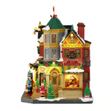 Tidings and Joy Toy Shop Lemax visto di lato, con vetrina illuminata, insegna “Joy Classic Toys & Dolls”, decorazioni natalizie, neve e personaggi davanti all’ingresso.