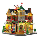 Tidings and Joy Toy Shop Lemax, negozio di giocattoli natalizio illuminato con facciata rossa, vetrine decorate, neve sul tetto, alberelli, schiaccianoci e Babbo Natale.