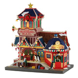 Stazione ferroviaria natalizia Lemax innevata e illuminata, con biglietteria, torre con stella, personaggi, pinguini, valigie e dettagli decorativi.