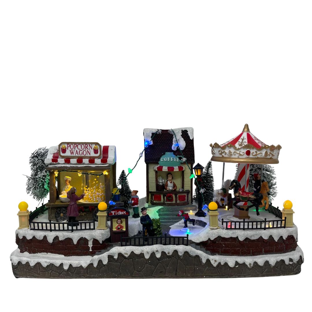 Villaggio natalizio luminoso a tema luna park con giostra, bancarella di popcorn e chiosco del caffè, decorato con luci LED multicolore e personaggi in miniatura.