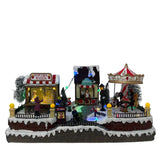 Villaggio natalizio luminoso a tema luna park con giostra, bancarella di popcorn e chiosco del caffè, decorato con luci LED multicolore e personaggi in miniatura.