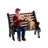 Personaggi Lemax Lunchbreak Buddy con ragazzo seduto su una panchina mentre mangia un panino, accanto al suo cane che lo osserva.