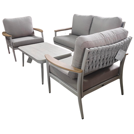 Salotto da esterno con divano, due poltrone e tavolino con struttura in metallo e cuscini grigio chiaro.