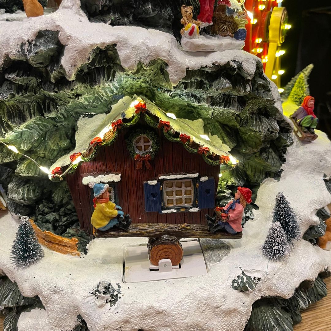 Dettaglio di una casetta in legno nel villaggio natalizio, con personaggi e decorazioni luminose tra la neve.