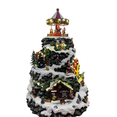 Villaggio natalizio decorativo a forma di montagna innevata con case illuminate, personaggi e giostra in cima.