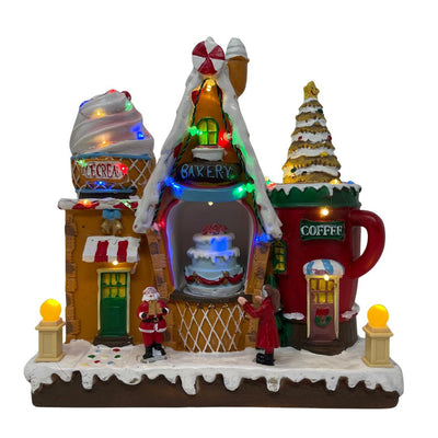 Negozio di dolci natalizio luminoso con casette a tema pasticceria, gelateria e caffè, decorato con luci LED multicolore e figure di Babbo Natale e una bambina.