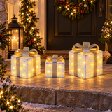 Tre pacchi regalo luminosi di diverse dimensioni, disposti davanti a un ingresso decorato con ghirlande natalizie