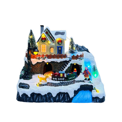 Paesaggio natalizio in miniatura con casa illuminata, trenino che attraversa gallerie innevate, figura di bambino e decorazioni con luci LED colorate.