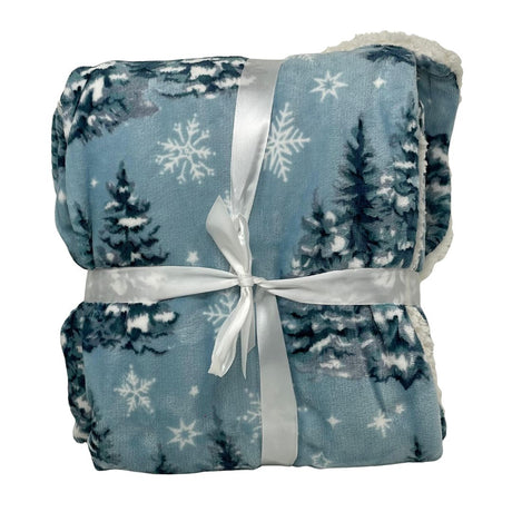 Plaid azzurro con stampa di alberi innevati e fiocchi di neve bianchi, piegato e legato con un nastro bianco.