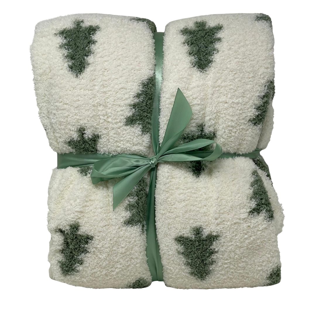 Plaid in tessuto morbido color bianco con motivo di alberelli verdi, piegato e legato con nastro verde.