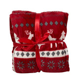 Plaid in pile rosso con decorazioni natalizie bianche e grigie raffiguranti renne, alberi e fiocchi di neve, legato con nastro rosso.