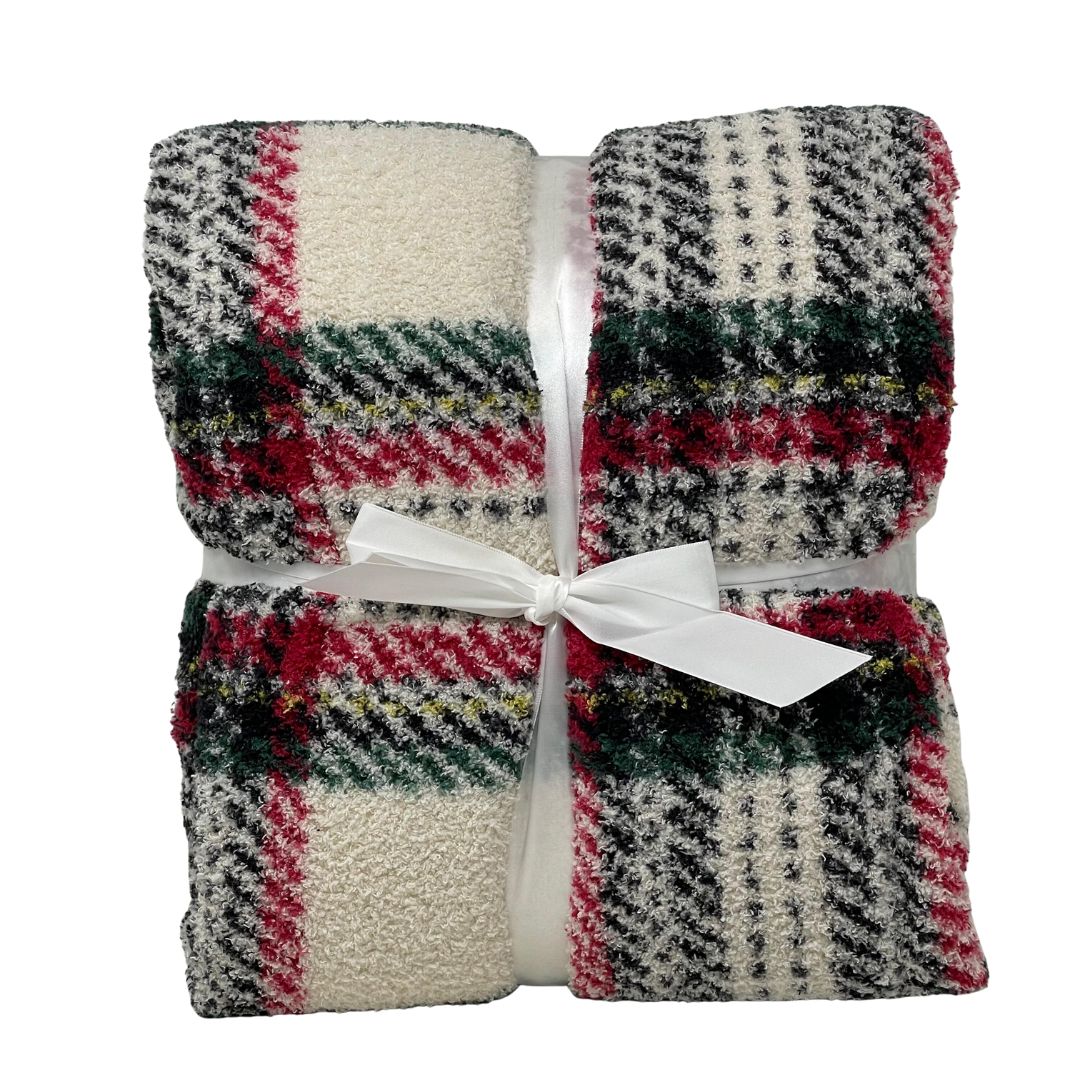 Plaid in morbido tessuto con fantasia scozzese nei toni del rosso, verde, nero e bianco, piegato e legato con un nastro bianco a fiocco.