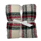 Plaid in morbido tessuto con fantasia scozzese nei toni del rosso, verde, nero e bianco, piegato e legato con un nastro bianco a fiocco.