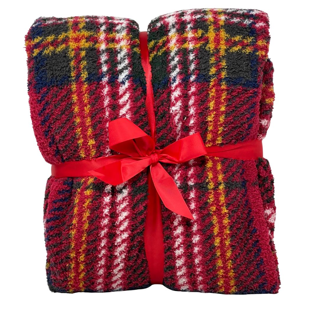 Plaid in morbido tessuto con fantasia scozzese nei toni del fucsia, verde, nero e bianco, piegato e legato con un nastro rosso a fiocco.