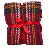 Plaid in morbido tessuto con fantasia scozzese nei toni del fucsia, verde, nero e bianco, piegato e legato con un nastro rosso a fiocco.