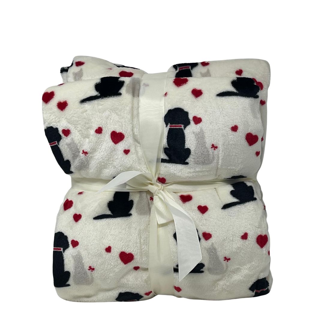 Plaid bianco con stampa di cani neri e beige circondati da cuori rossi, piegato e legato con nastro bianco.
