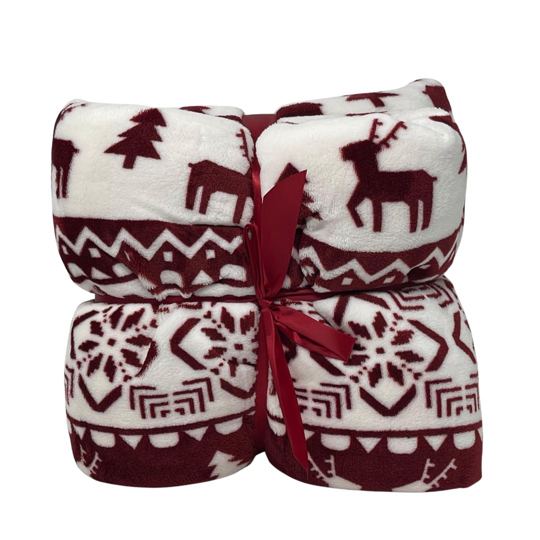 Plaid in pile bianco con disegni natalizi rosso scuro di renne, alberi e motivi geometrici, piegato e legato con nastro rosso.